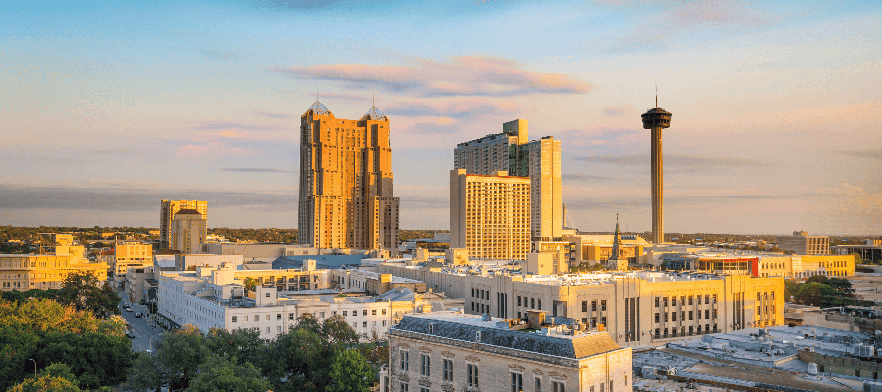 A picturesque view of downtown San Antonio at sunset, featuring prominent buildings and the iconic Tower of the Americas