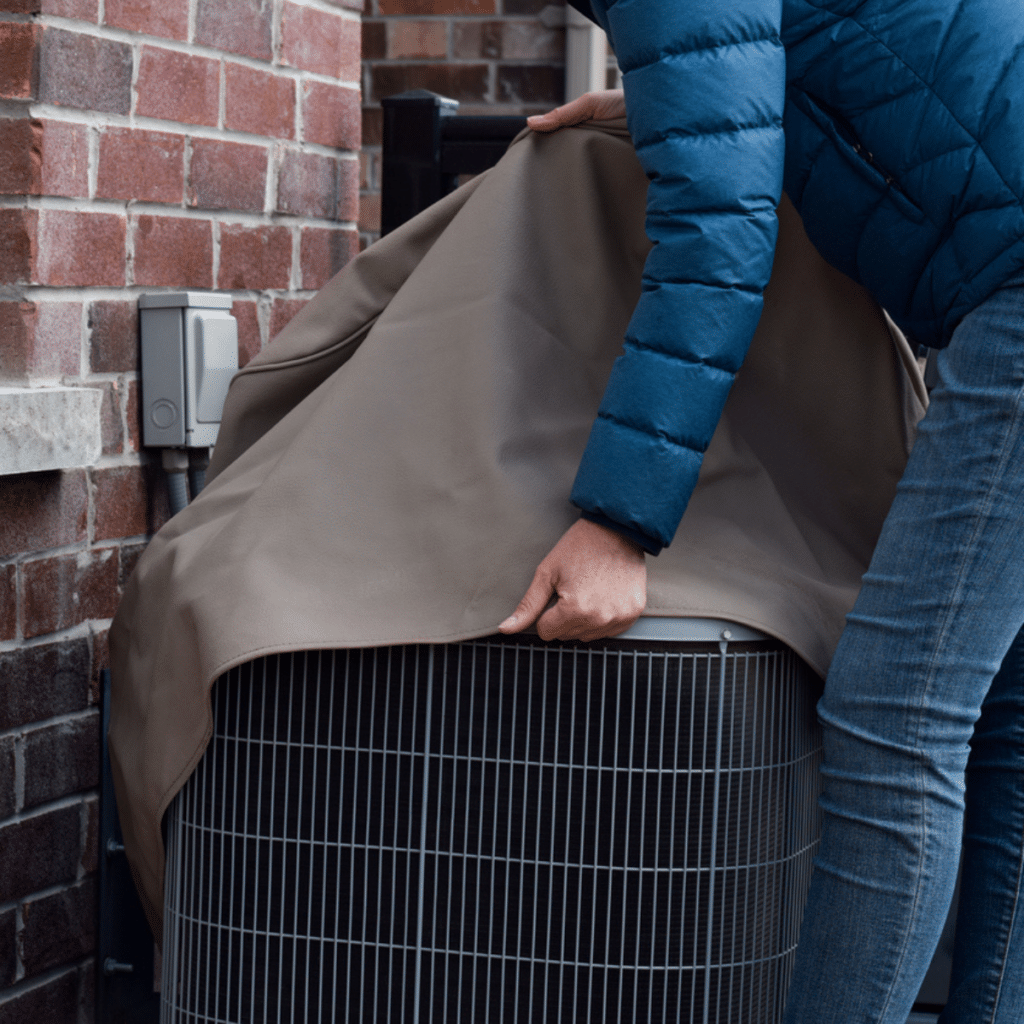 Person covering an outdoor AC unit with a protective cover