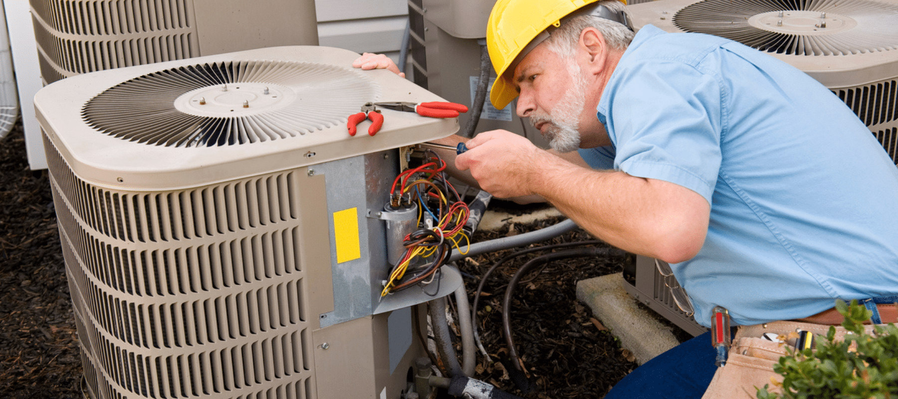 Technician repairing an outdoor AC unit with tools and wires exposed