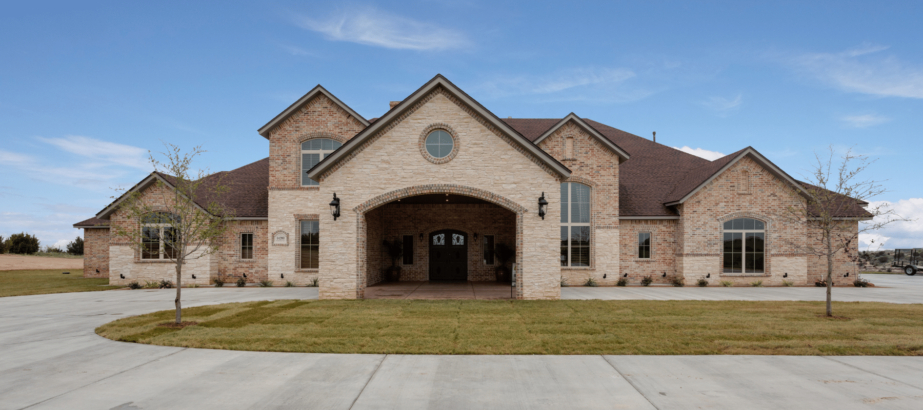 A spacious modern brick home with a circular driveway under a clear blue sky