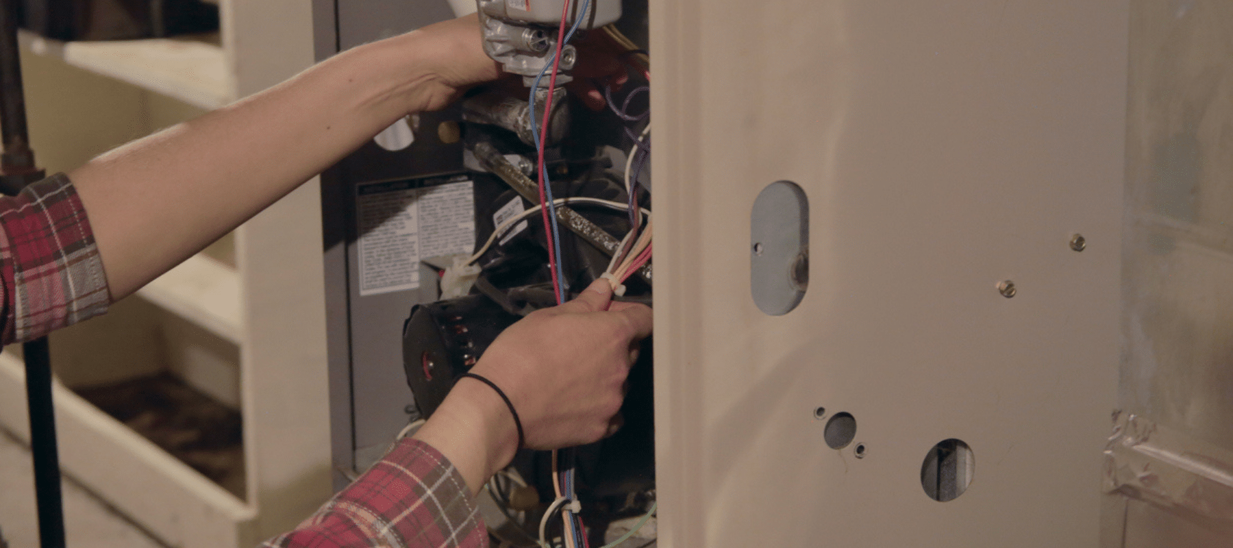 Hands adjusting wiring in the interior of a furnace